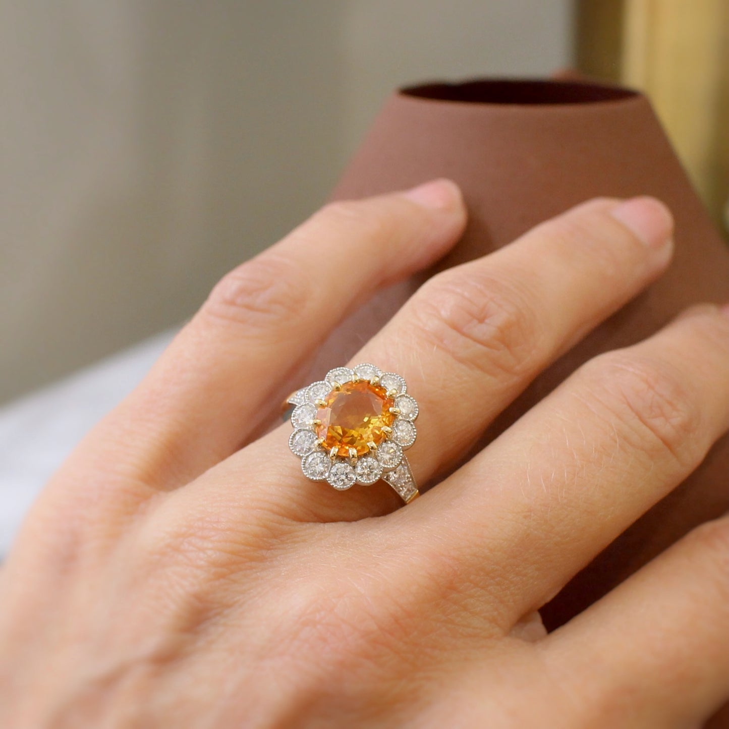 bague de fiançailles marguerite ornée d'un saphir orange rare de plus de 3 carats. entourage de diamants en serti semi-clos perlé