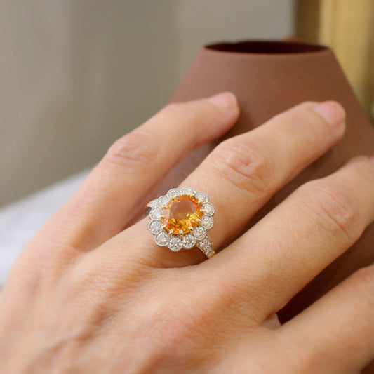 bague de fiançailles marguerite ornée d'un saphir orange rare de plus de 3 carats. entourage de diamants en serti semi-clos perlé